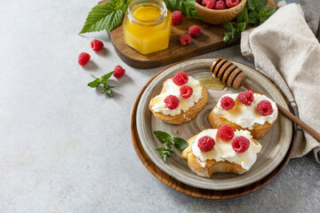 Fototapeta na wymiar Healthy summer breakfast with sweet sandwiches with ricotta, raspberries and honey on a stone table. Copy space.
