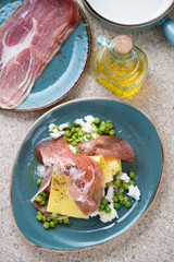 Pea, ricotta and prosciutto open lasagna served on a turquoise plate, above view on a beige marble background, vertical shot