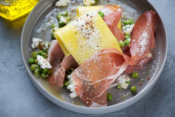 Open lasagna with prosciutto, ricotta cheese and crushed green peas in a grey plate, close-up, selective focus