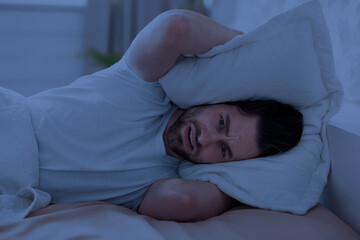 Guy in bed covering his head with pillow