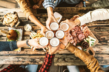 Fototapeta Friends cheering beer glasses on wooden table covered with delicious food - Top view of people having dinner party at bar restaurant - Food and beverage lifestyle concept obraz