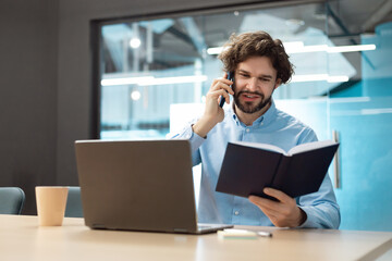 Business man talking on phone at office, reading diary