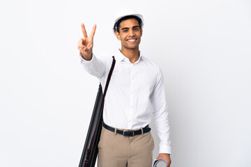 African American architect man with helmet and holding blueprints over isolated white background _ smiling and showing victory sign