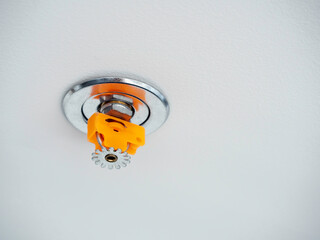 Close-up fire sprinkler, chrome and plastic orange color materials isolated on white ceiling...