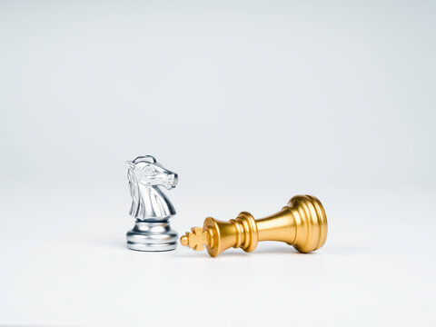 The silver horses, knight chess piece standing near the loser golden king chess piece who fell isolated on white background. Leadership, winner, loser, competition, and business strategy concept.