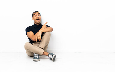 Fototapeta premium African American man sitting on the floor surprised and pointing side