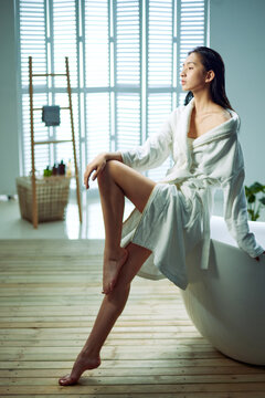 Young woman sitting in bath crock edge, wearing a bathrobe