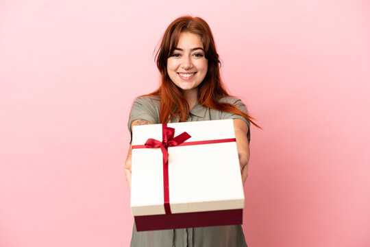 Young redhead caucasian woman isolated on pink background pregnant and holding a gift
