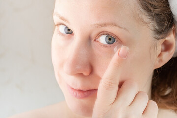 woman puts on contact lenses, holds on her finger