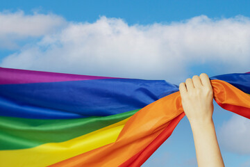 Lgbt flag in hand on sky background,same sex love, solidarity with homosexuals, and support for transgender rights concept