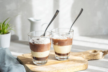 Three-layer chocolate and vanilla mousse dessert in glass cups, sprinkled with coconut flakes, on a children's serving board. brunch