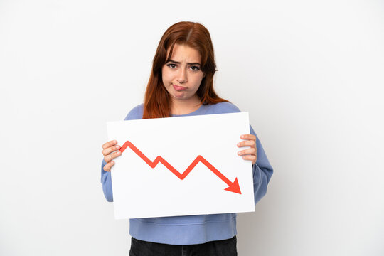 Young redhead woman isolated on white background holding a sign with a decreasing statistics arrow symbol with sad expression