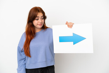 Young redhead woman isolated on white background holding a placard with arrow symbol