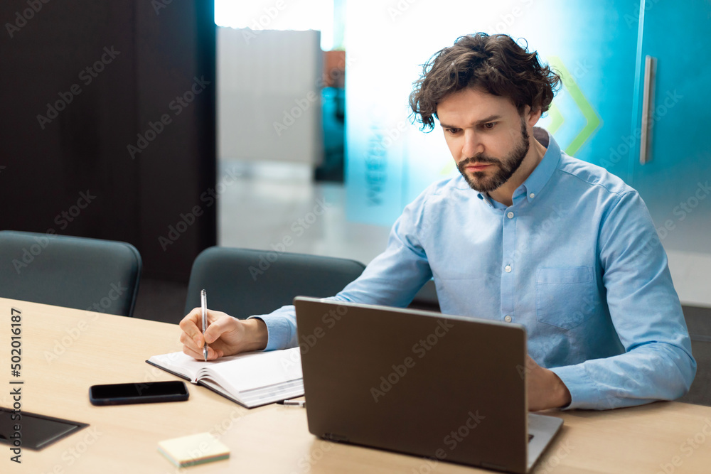 Poster portrait of focused man using laptop and writing in notebook