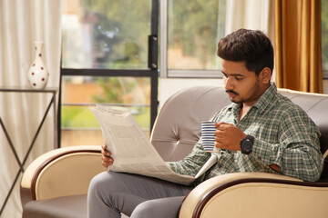 Indian Man reading newspaper and drinking tea, sitting on couch