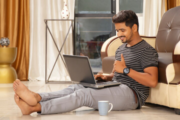 Happy Indian Man doing thumbs up and looking in laptop, while sitting on floor
