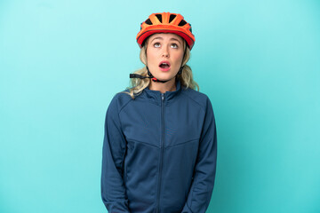 Young cyclist woman isolated on blue background looking up and with surprised expression
