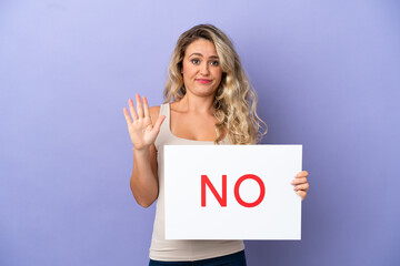 Naklejka premium Young Brazilian woman isolated on purple background holding a placard with text NO and doing stop sign