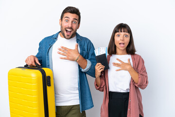 Young traveler couple holding a suitcase and passport isolated on white background surprised and shocked while looking right