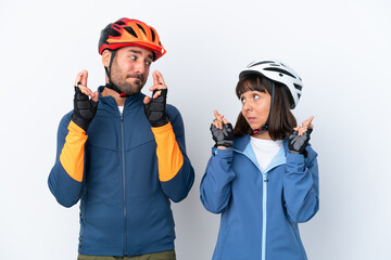 Young cyclist couple isolated on white background with fingers crossing and wishing the best