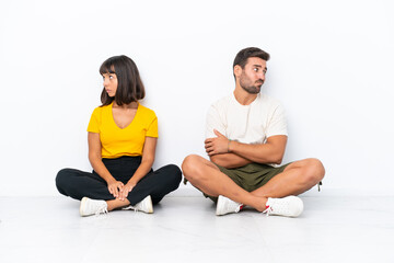 Fototapeta na wymiar Young couple sitting on the floor isolated on white background with confuse face expression while bites lip