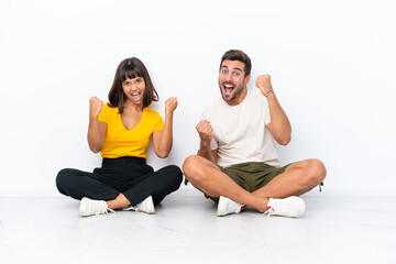 Fototapeta na wymiar Young couple sitting on the floor isolated on white background celebrating a victory