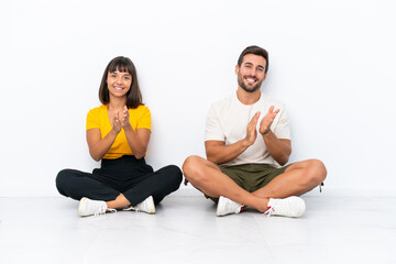 Young couple sitting on the floor isolated on white background applauding after presentation in a conference