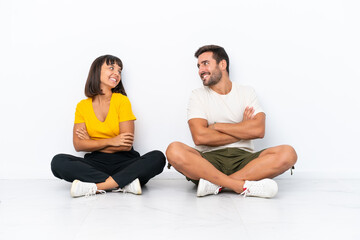 Obraz premium Young couple sitting on the floor isolated on white background looking over the shoulder with a smile