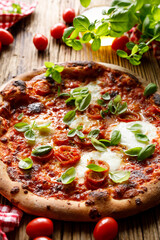 Pizza margarita with mozzarella cheese and tomatoes sprinkled with fresh basil leaves on a wooden board, close-up view