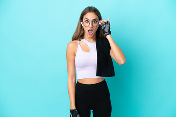 Young sport woman isolated on blue background with glasses and surprised