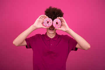 Sport and retro style. Young attractive guy on a pink background with dumbbells and a donut.