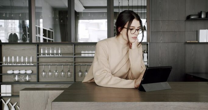 Beautiful woman at home using digital tablet in modern kitchen room and loft apartment. ooking digital tablet for follow news, work and social media online in loft kitchen at home