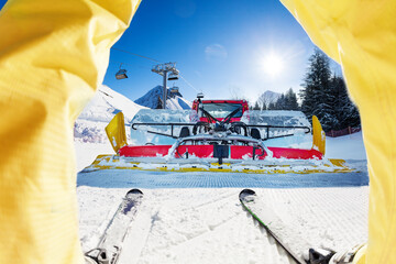 Between legs shoot of skier against snow grooming tractor