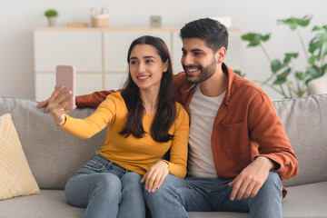 Obraz premium Happy Arabic Spouses Making Selfie Using Mobile Phone Indoor