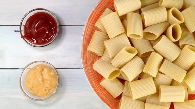 Uncooked raw italian paccheri pasta rotating slowly on turntable in dish.
