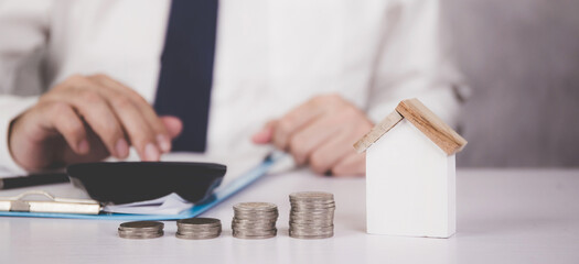 Fototapeta premium Businessman calculate with calculator about investment and having document on clipboard and home model on desk, insurance and finance, planning about real estate and residential, business concept.