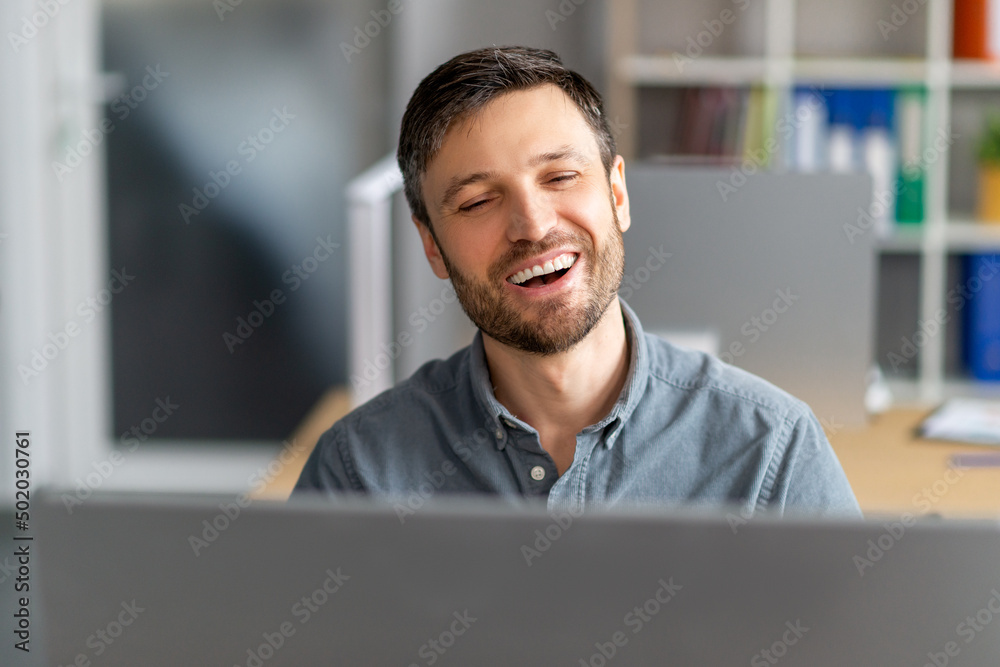 Wall mural Portrait of happy mature male manager working on computer, having video call and smiling at screen