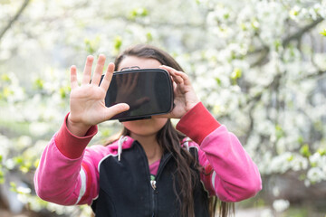 Happy amazed little girl wearing virtual reality goggles watching movies or playing video games. Cheerful surprised child looking in VR glasses and gesturing