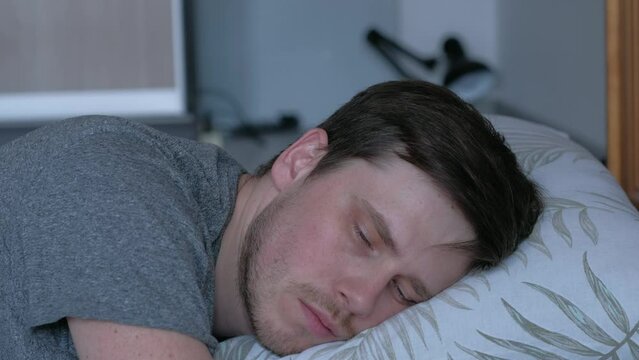 Depression caused by isolation during quarantine. On the bed covered with bed linen, on a pillow lies a man, he looks indifferently at one point.