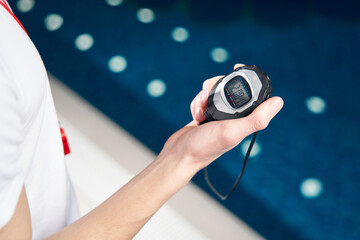 Male hand is holding a timer chronometer in the background at the swimming pool