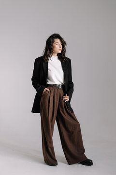 Attractive woman wear business look. Brunette model wear white shirt, black men's jacket and brown baggy pants. Winter, fall autumn or spring minimal outfit.