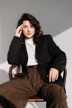 Fashion studio photo of stylish European brunette woman in in long baggy pants and a black jacket posing on white background. Trendy office style in clothes.