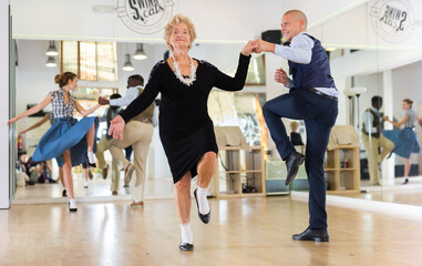 Man and elderly woman performing jazz dance in dancing room