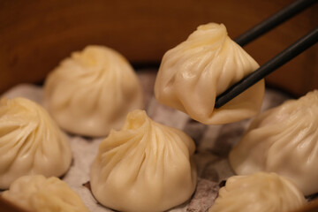 extreme close up of chopsticks picking up Tangbao (soup bun) in steamer. soup-filled of steamed buns (baozi) in Chinese cuisine