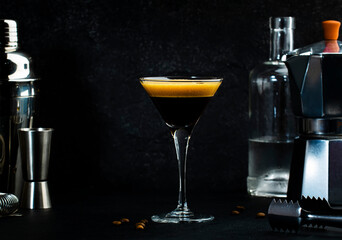 Classic alcoholic cocktail Espresso martini with vodka, coffee liqueur, syrup and ice in glass on dark counter background,  bar tools, negative space