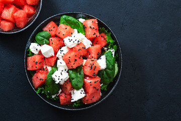 Summer Watermelon juicy salad bowl with feta cheese, spinach and black sesame seed, dark table background, top view, negative space