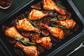 Baked chicken legs, drumsticks with sweet figs and onions in balsamic marinade on black baking sheet, rusty green table background, top view