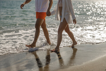 Cropped shot of young couple walking through waves on beach holiday