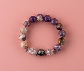 Bracelet made of amethyst and quartz,. A bracelet made of natural stones on the hand. Handmade jewelry on a pink background.
