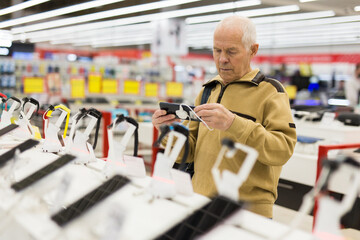 elderly man examines tablet computer in showroom of electronics store